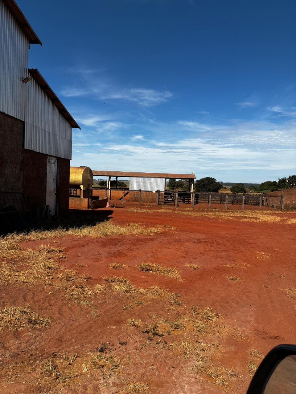A farm yard with a metal barn, a fuel storage tank and a covered cattle corral.