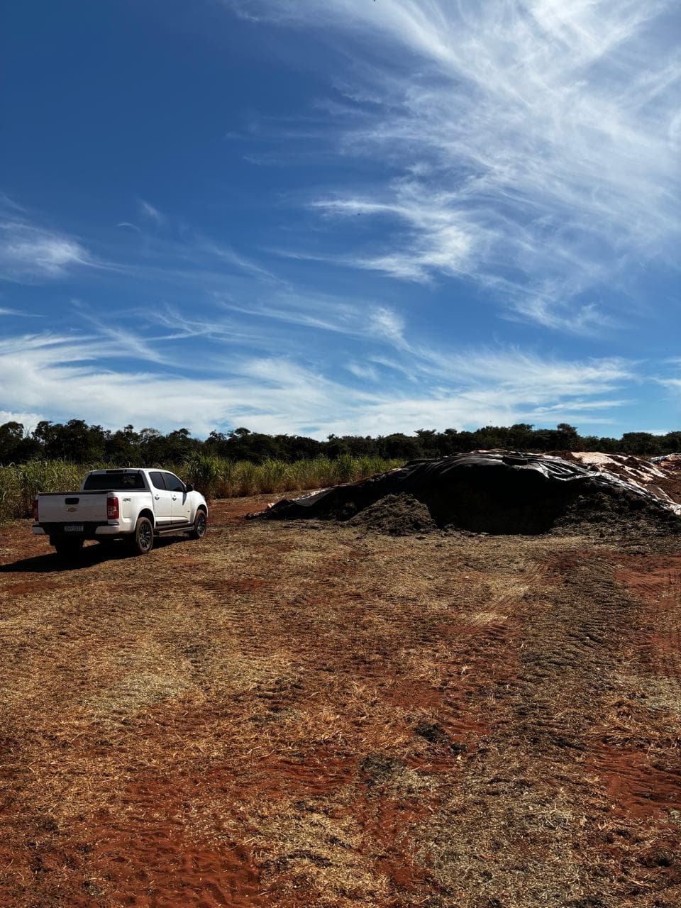 A covered silage pile in a field next to a parked pickup truck.