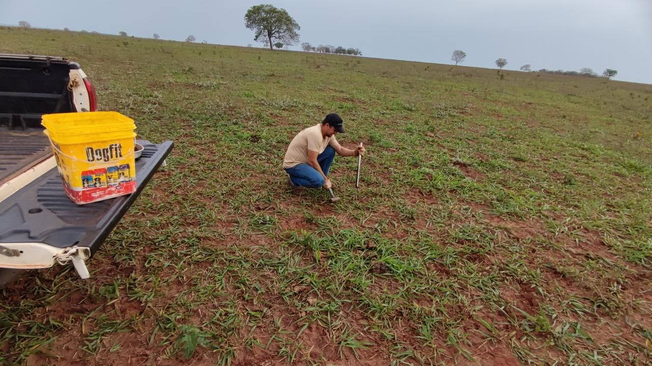A technician kneeling to collect a soil sample with an auger beside a pickup truck during field assessment.