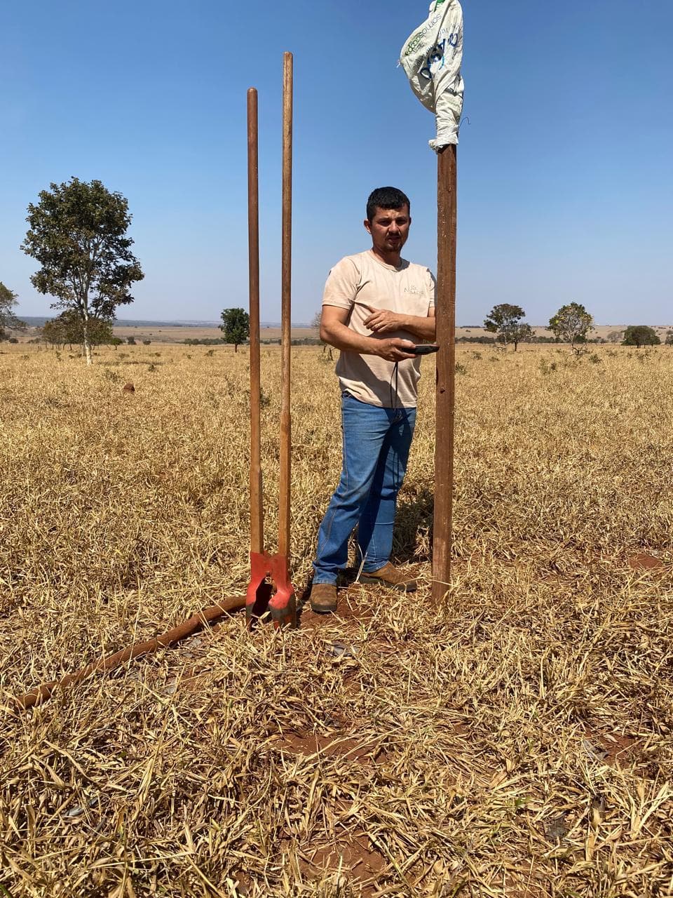 A technician standing in a dry pasture with soil-probe tools and a sample bag during the initial soil survey.