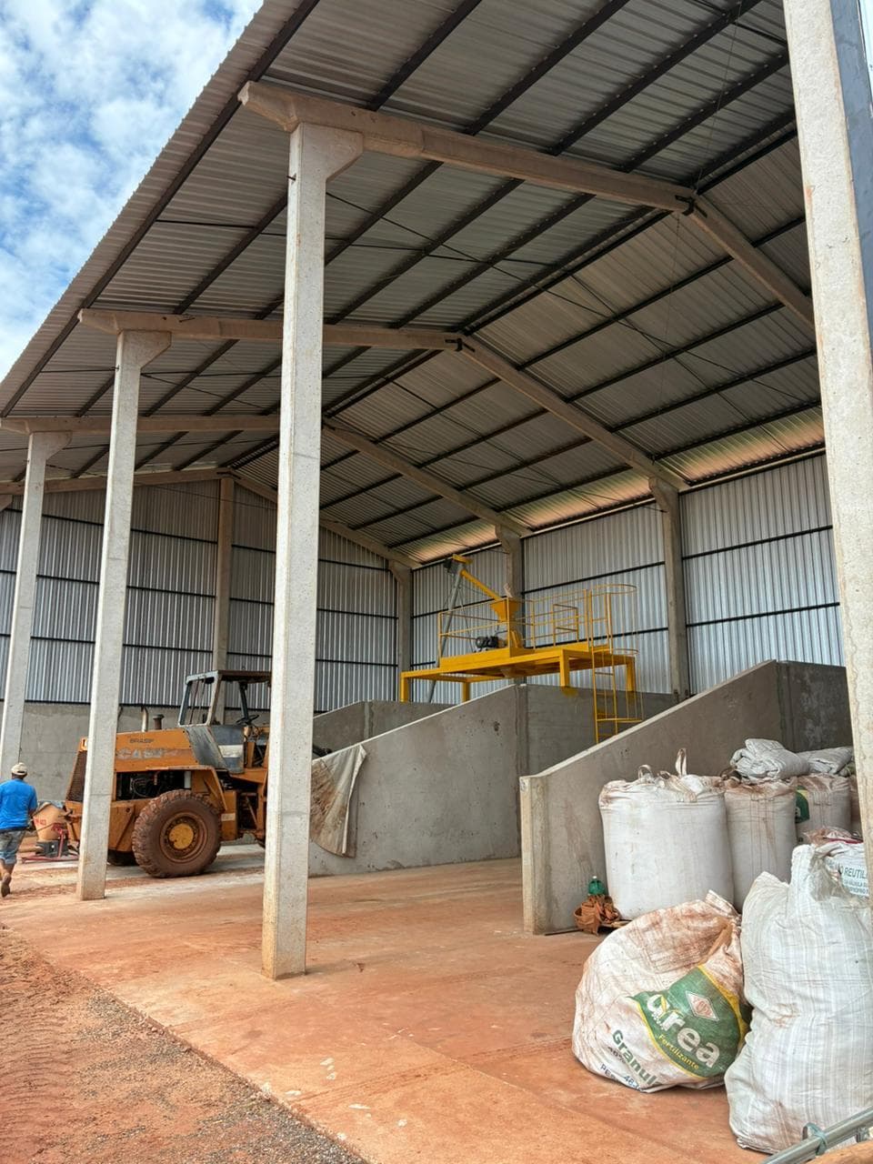 Interior of the fertilizer and input storage building, under construction, with loader and stacked bags.